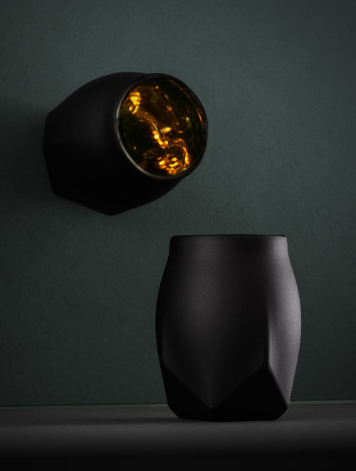 The Norlan Whisky Glass VAILD BLACK shown against the background of a tilted mirror that provides an image in which both the front of the glass and a top view of the glass are both in the same image frame.